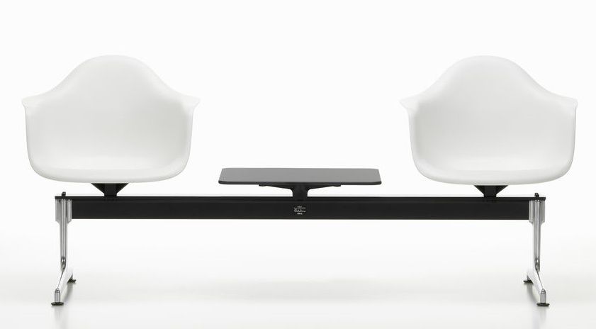 Zwei weiße Eames Plastic Armchairs auf schwarzer Traverse von Vitra mit kleinem Tisch.