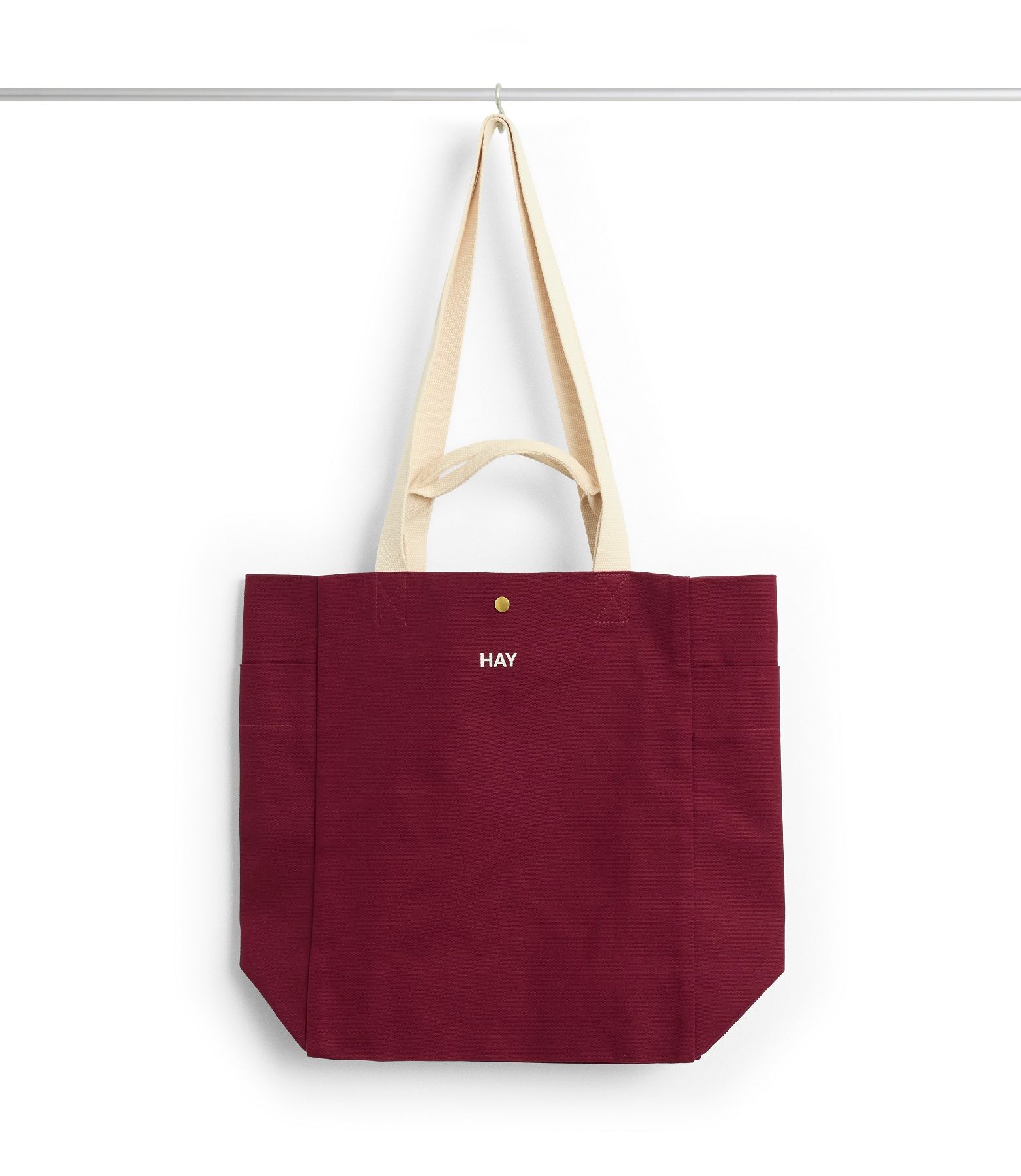 Weinrote Hay Everyday Tote Bag aus Baumwolle mit beigen Trägern hängt an einem Haken.