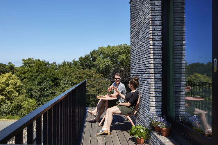 Extremis Bistroo Stuhl und Tisch Outdoor-Set auf Balkon mit Paar, das Getränke genießt.