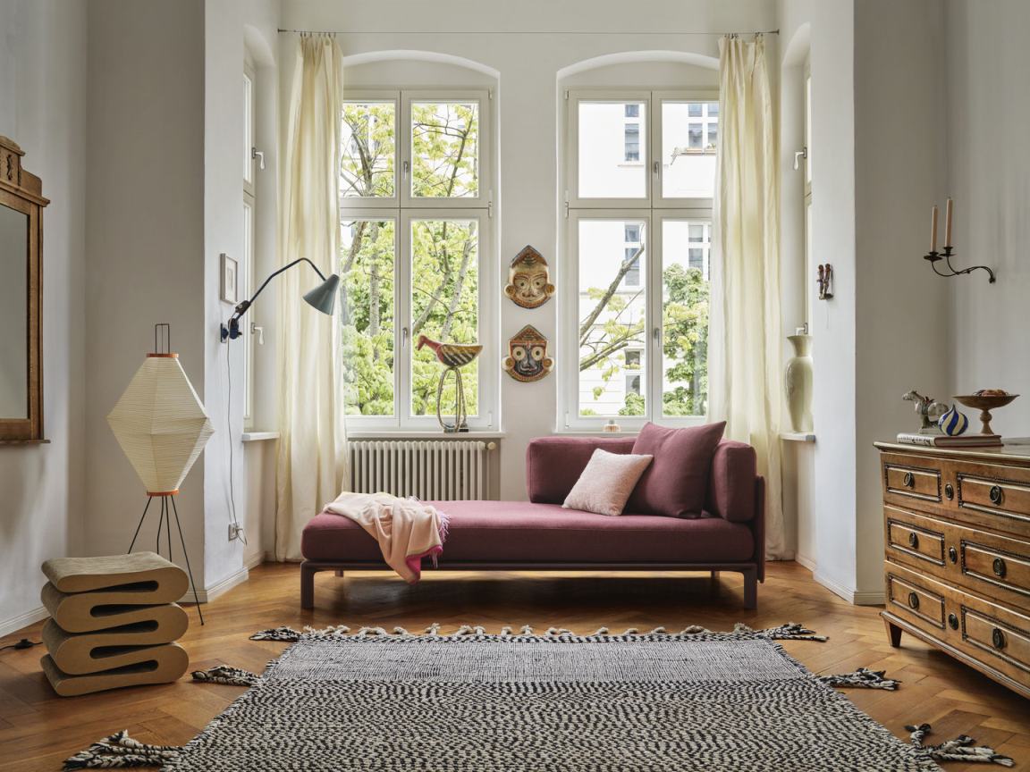 Wohnzimmer mit Vitra Anagram Sofa Plattform in Pflaume, Teppich, Kommode und Tageslicht für gemütliches Ambiente.