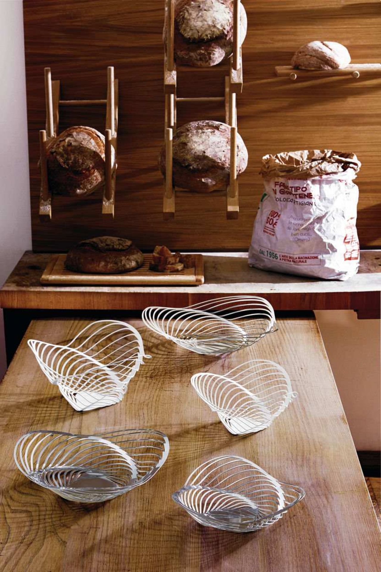 Fünf moderne Alessi ACO Trinity Schalen aus Metalldraht auf einem Holztisch, Brot im Hintergrund.