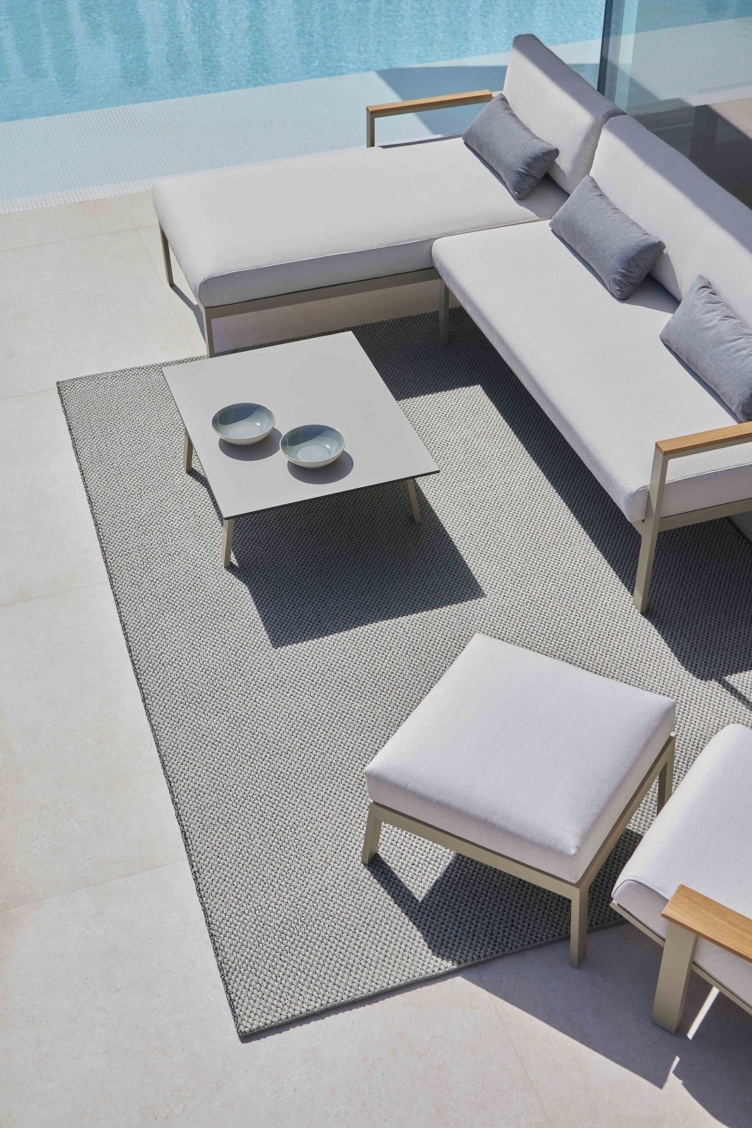 Saline Outdoor Rug Teppich Gan in Grau, kombiniert mit weißen Gartenmöbeln und Pool.