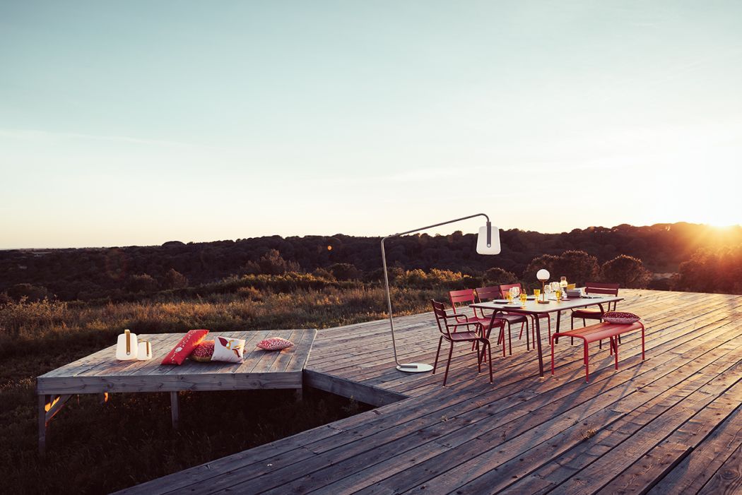 Luxembourg Tisch von Fermob, rotes Outdoor-Tischset auf Holzterrasse bei Sonnenuntergang. Gartenmöbel für Terrasse.