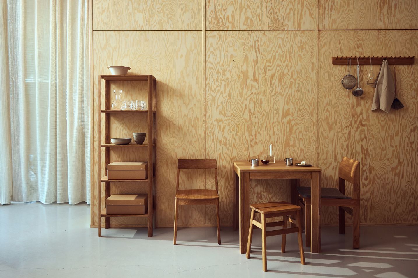 Esszimmer mit Form & Refine Stuhl, Holztisch, Hocker und Regal vor einer Holzwand.