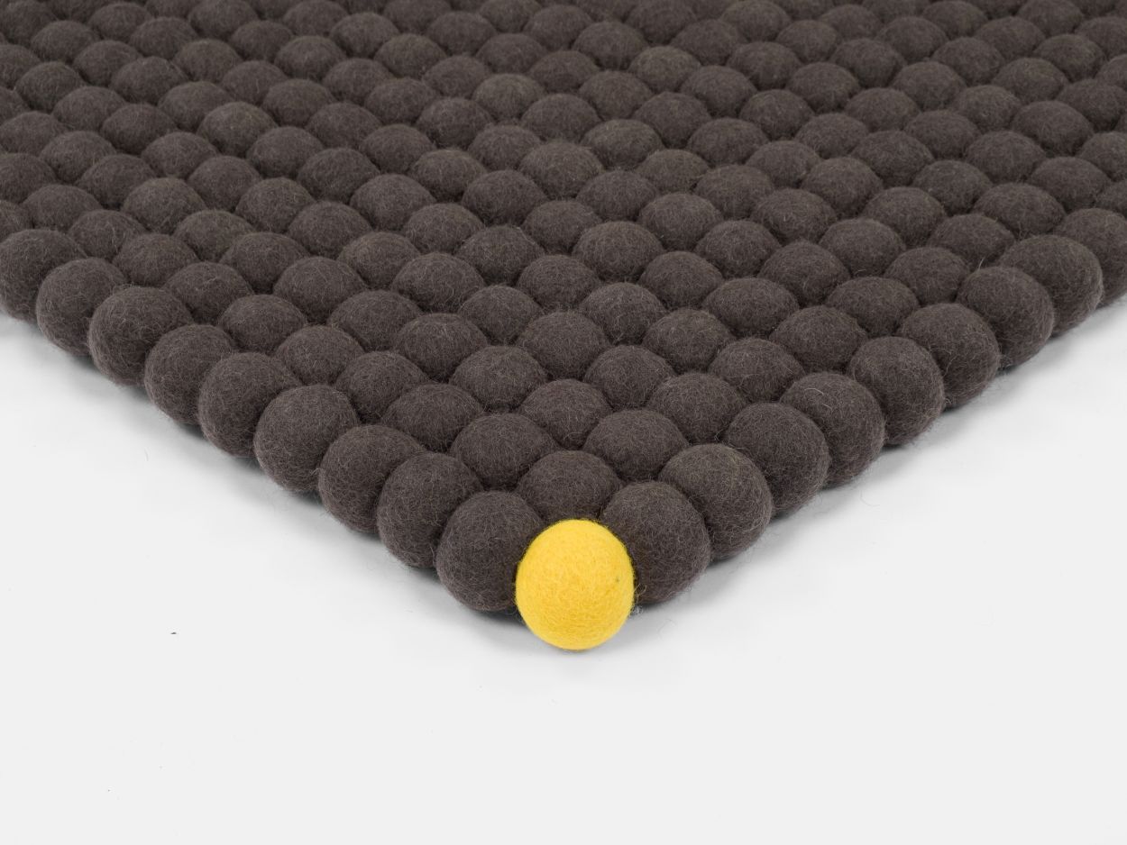 Detailansicht: Grauer Filzteppich "Big One" von myfelt (200x300 cm) mit gelber Filzkugel.