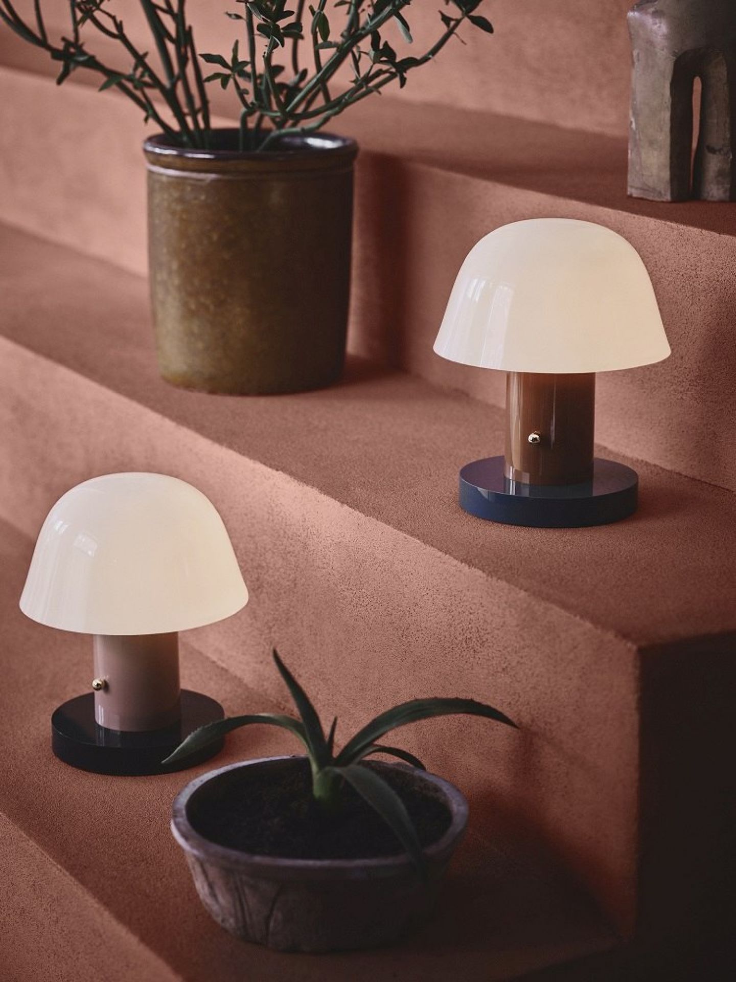 Zwei Setago Akkuleuchten von AndTradition auf einer Treppe, stimmungsvolle Tischleuchten im Pilzdesign.