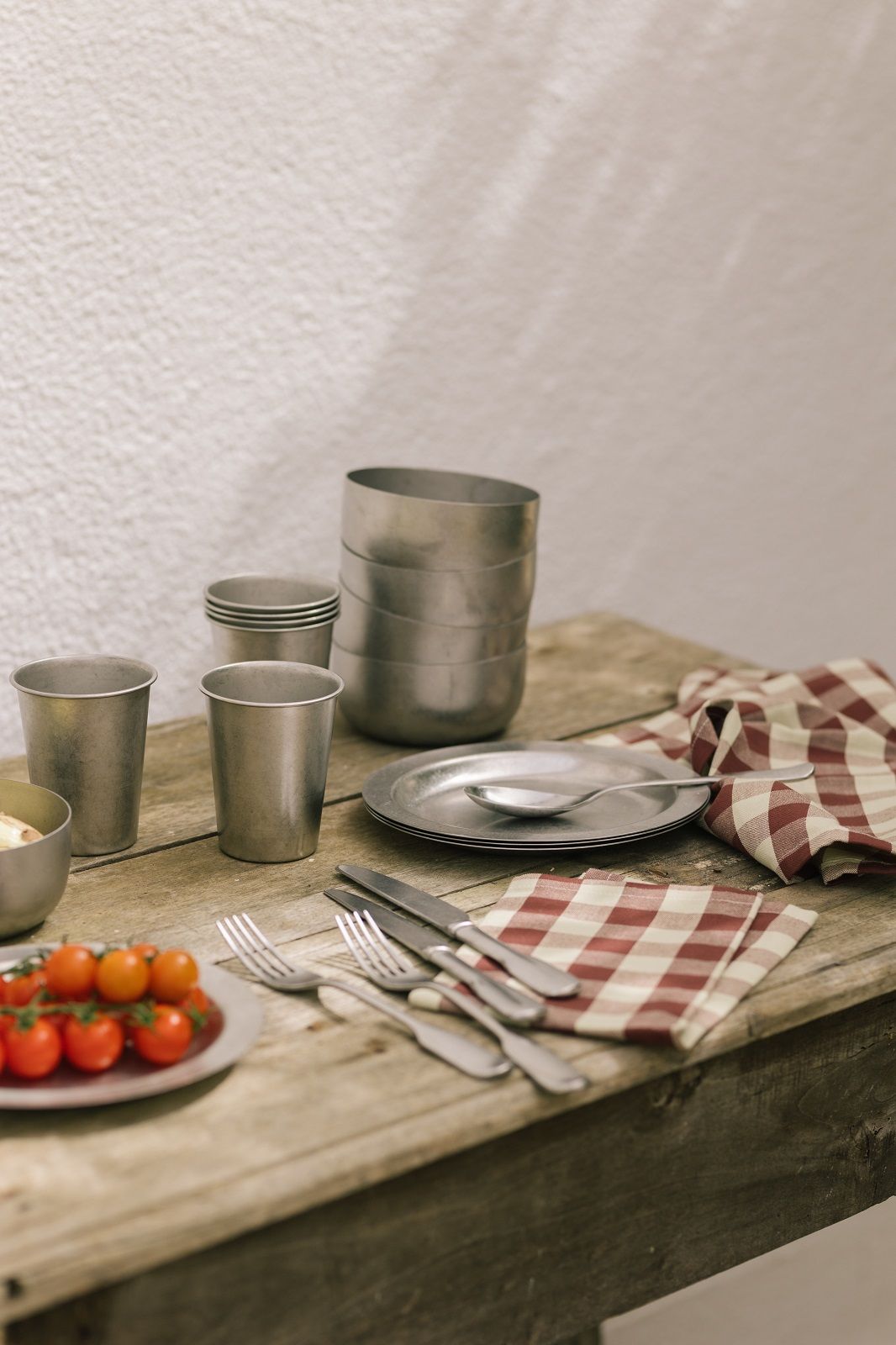 Ferm Living Tumbled Cup Campingtasse aus Metall mit Geschirr und Tomaten auf rustikalem Holztisch.