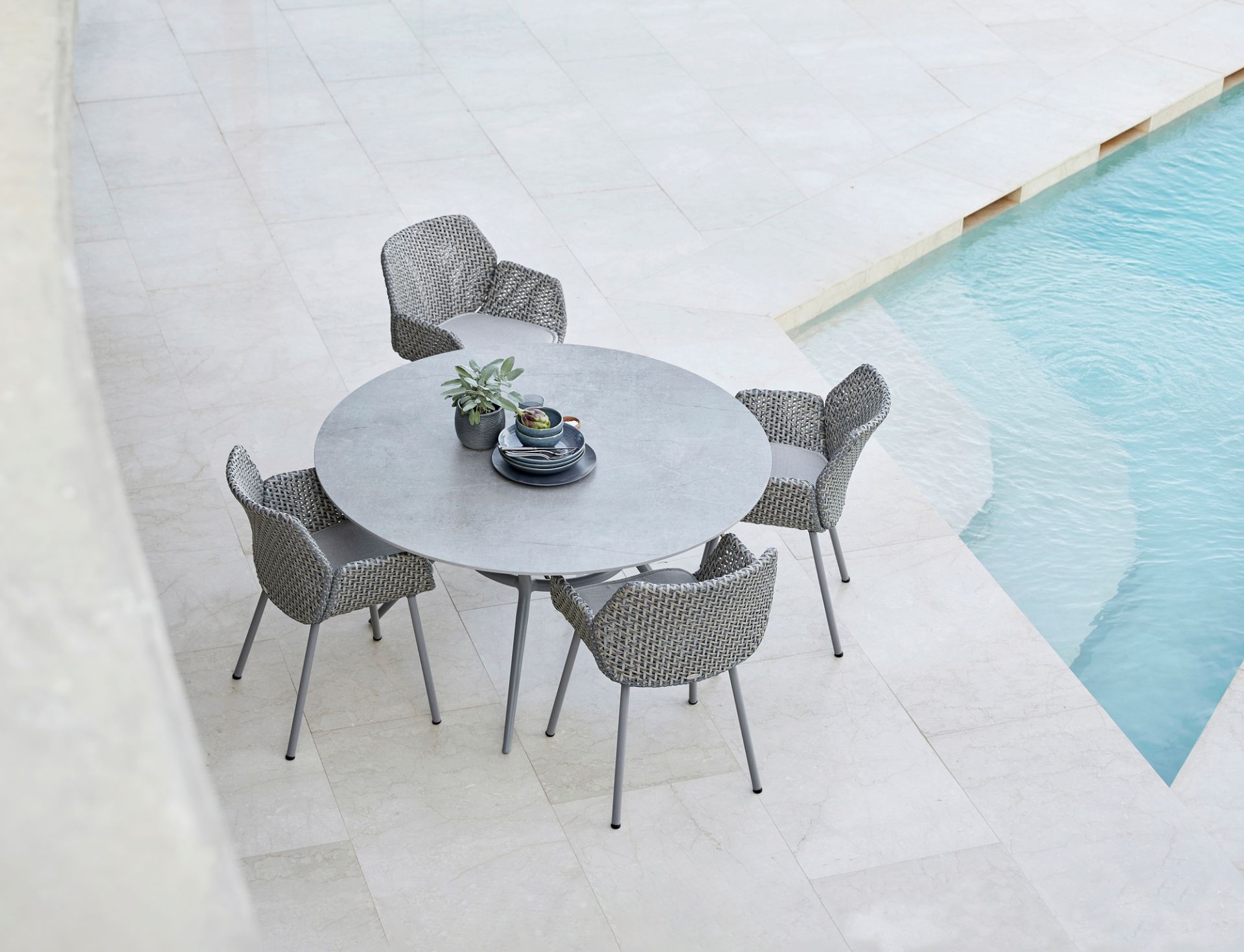 Cane-Line Vibe Sessel und runder Gartentisch aus grauem Geflecht am Pool für vier Personen.