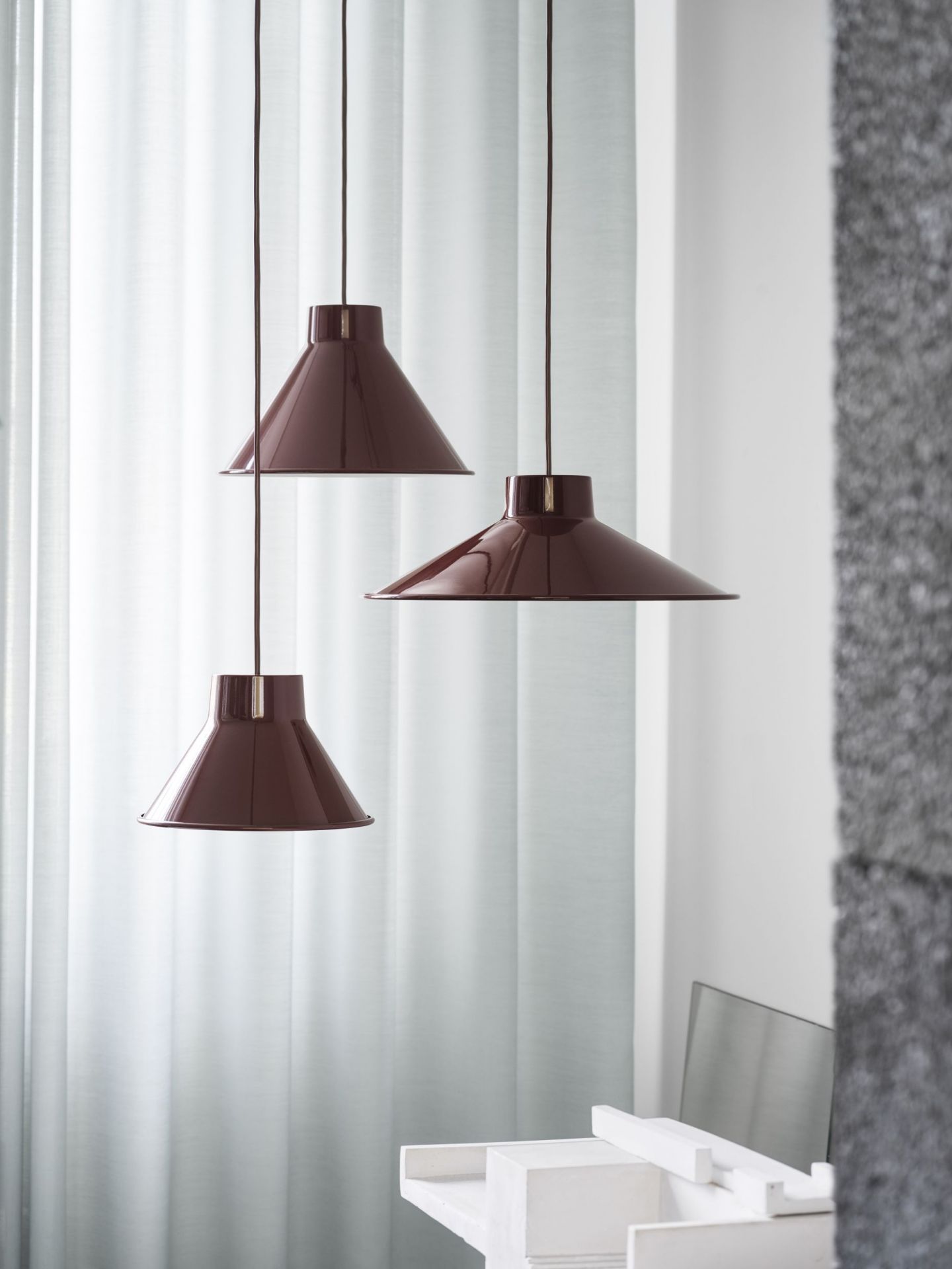 Drei Muuto Top Pendant Lamp Pendelleuchten in Grau hängen vor einem hellen Vorhang im Raum.