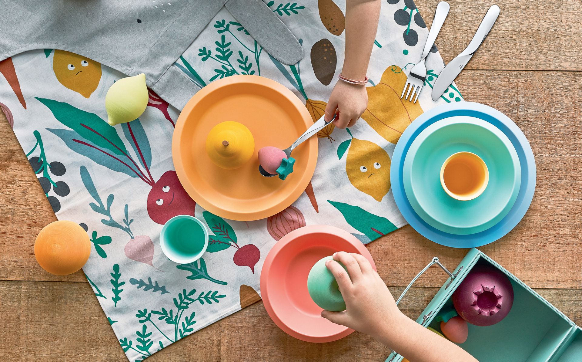 Buntes Alessi Kindergeschirr-Set auf einem Tisch mit Obst-Motiv, ideal für Kleinkinder.