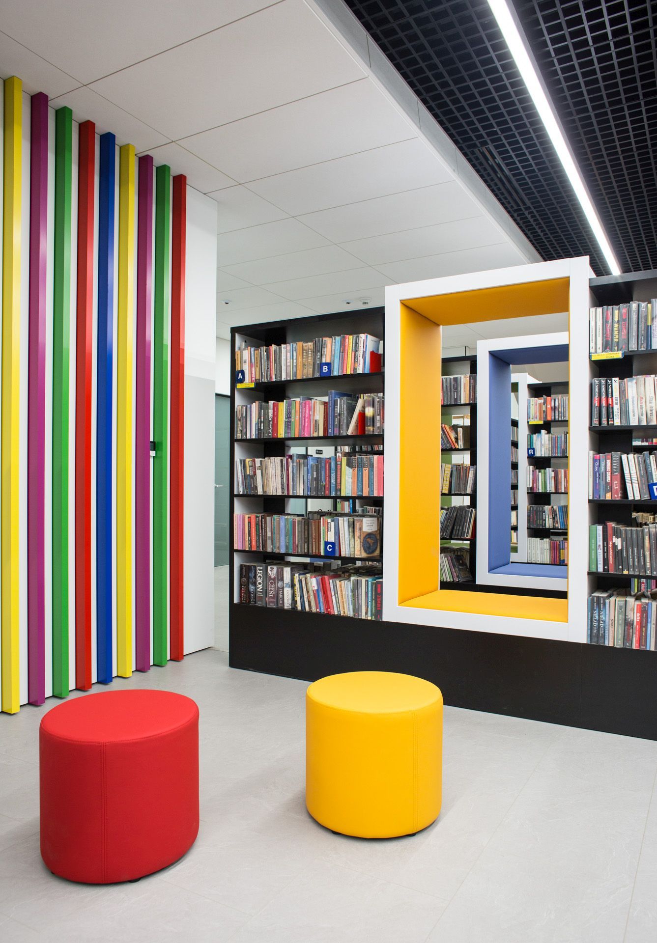 Roter und gelber Bejot point POP R 450 Pouf Sitzhocker auf Rollen in moderner Bibliothek.