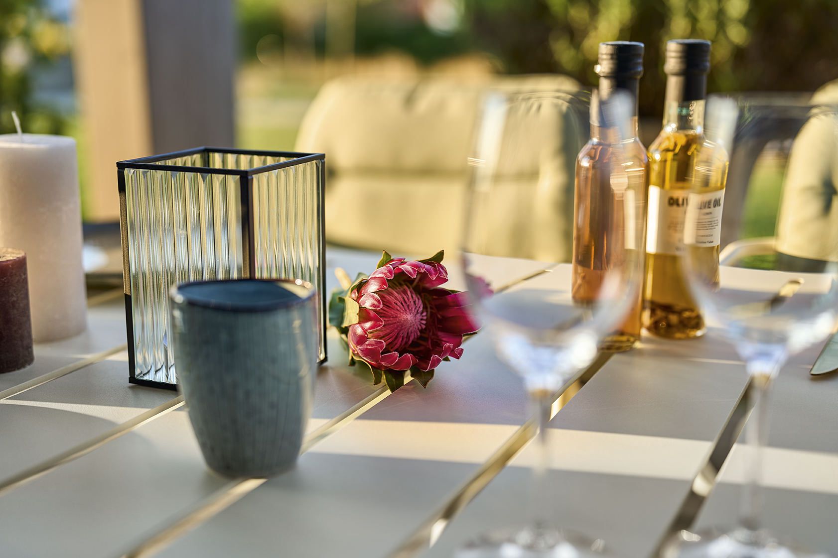 Detailaufnahme des Vapio Tisch Outdoor von Weishäupl, dekoriert mit Kerzen, Blume, Gläsern und Ölflaschen.