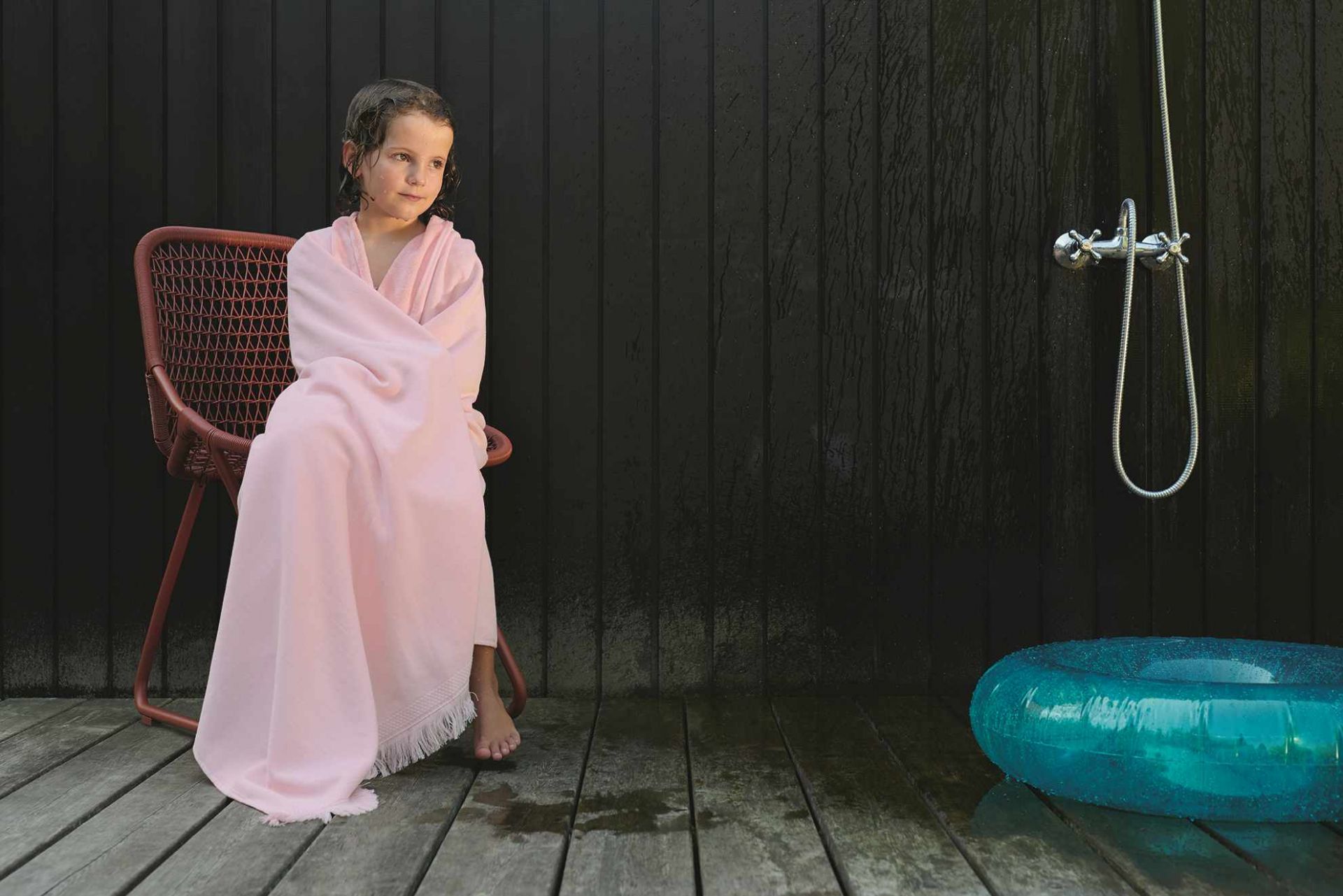Mädchen in Handtuch sitzt auf einem roten Sixties Outdoor Stuhl von Fermob.