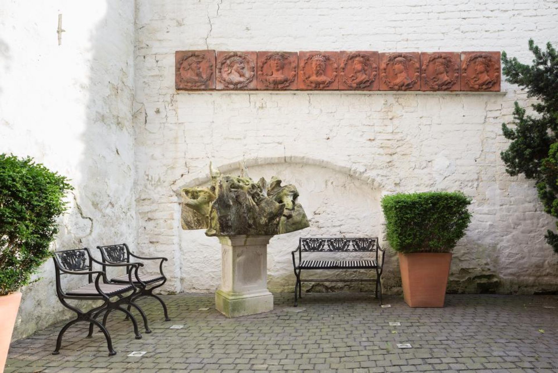 D60-2 Tecta Gartenbank aus Metall im Außenbereich mit Skulptur und Pflanzkübel.