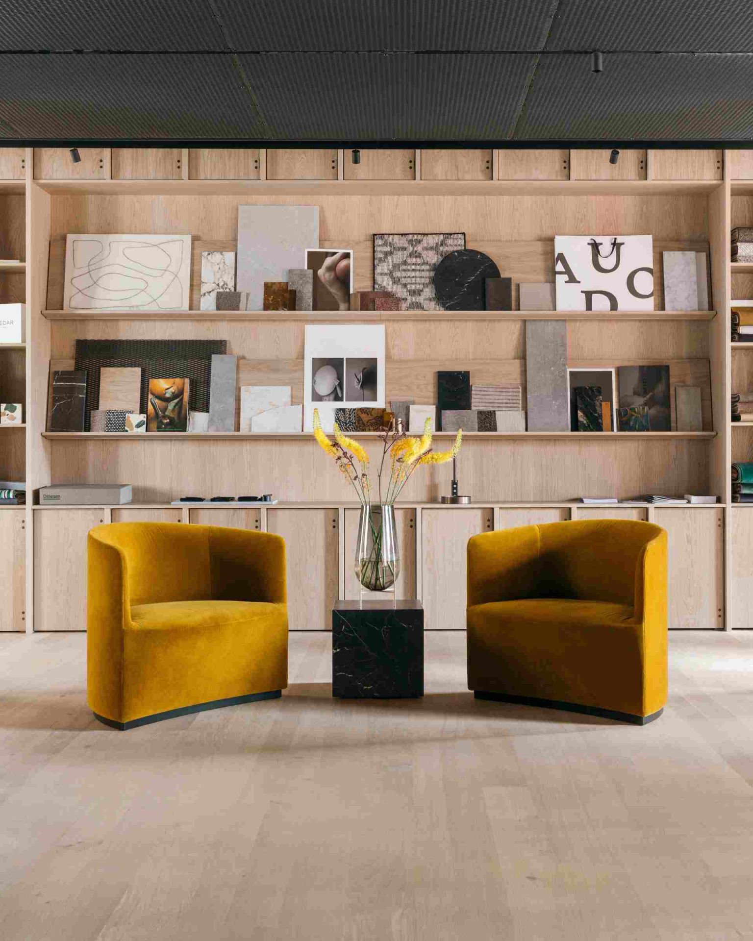 Audo Plinth Cubic Beistelltisch aus braun-grauem Kendzo Marmor zwischen zwei gelben Sesseln.