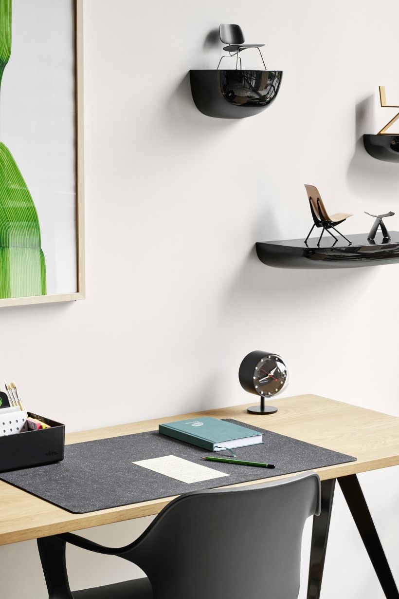 Schreibtischszene mit Vitra Night Clock Tischuhr in Schwarz, Notizbuch und Büromaterialien auf hellem Holztisch.