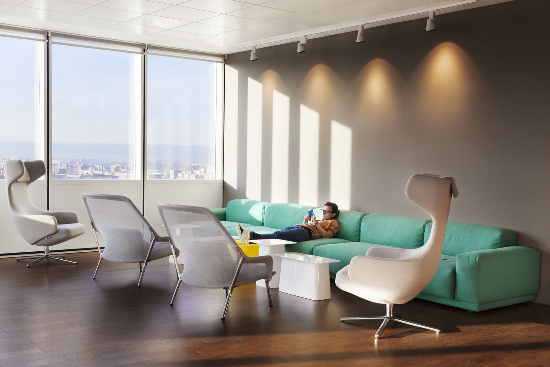 Helles Büro mit Grand Repos Sessel von Vitra und Person auf einem mintgrünen Sofa.