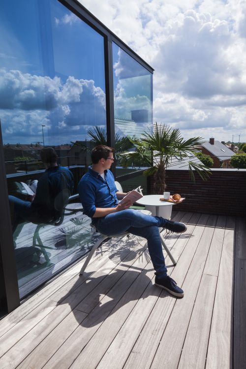 Mann liest auf dem Balkon sitzend am Bistroo Tisch von Extremis ein Buch.