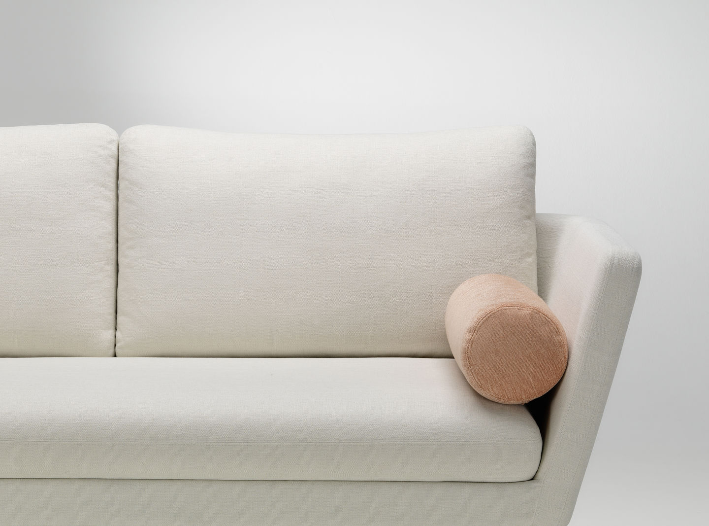 Nahaufnahme eines weißen Sofas mit großem Kissen und einem kleinen, runden Vitra Sofakissen in Apricot.