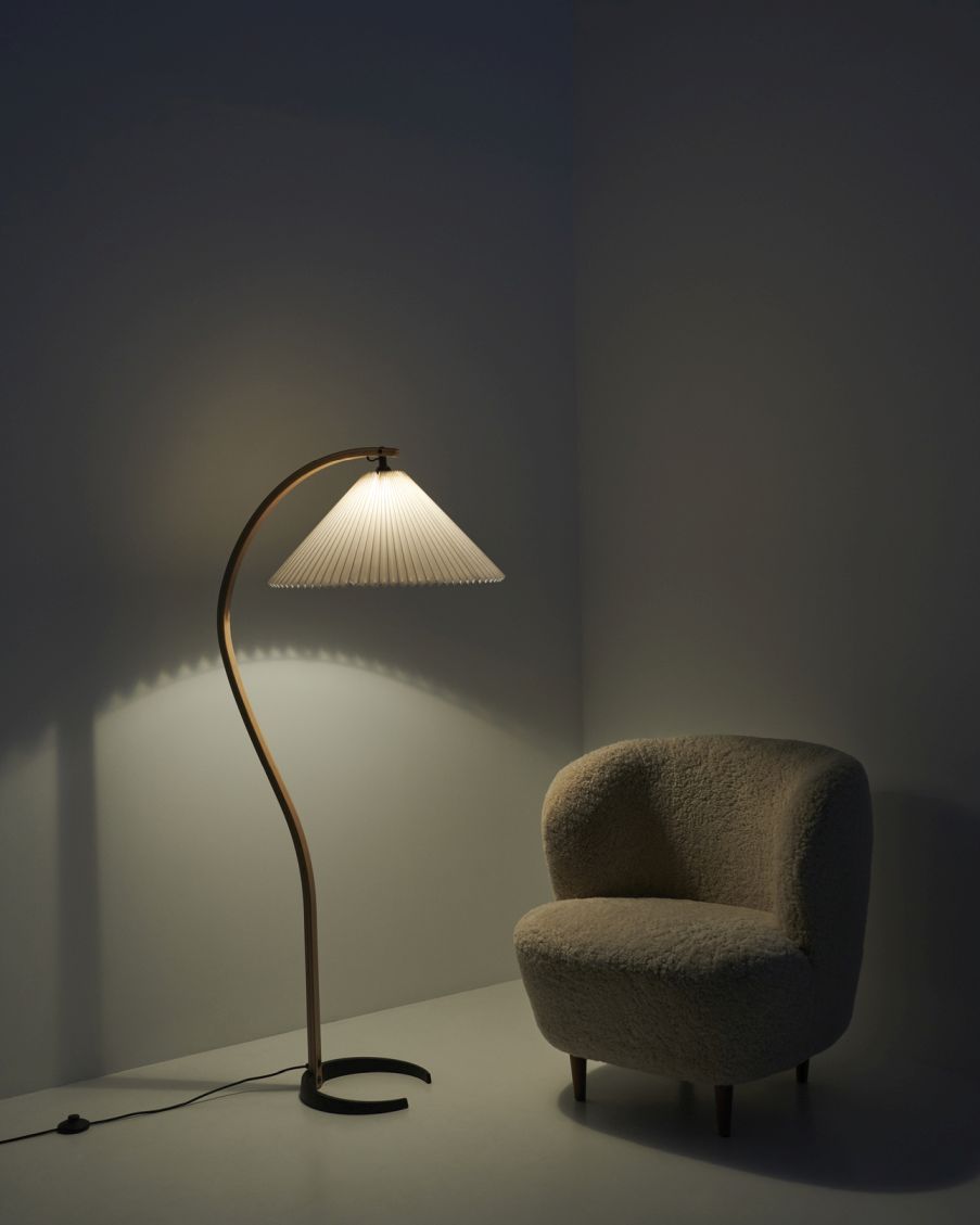 Elegante Timberline Stehleuchte von Gubi mit plissiertem Schirm und beigem Sessel in dunklem Raum.
