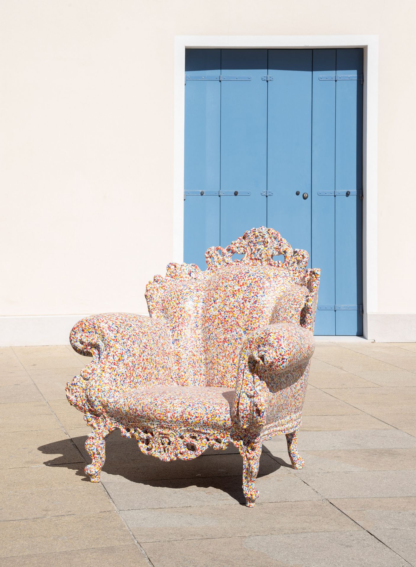 Magis Proust Sessel Outdoor, bunter Design Gartenstuhl vor blauer Tür und heller Fassade.