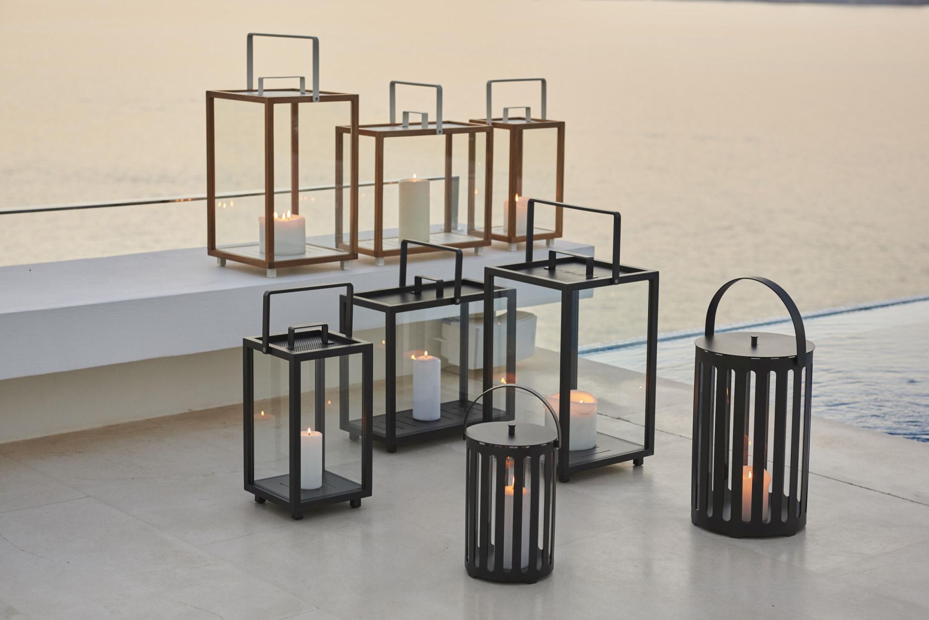 Verschiedene Cane-Line Laternen, inklusive der rechteckigen Lighthouse Teak Laterne, mit Kerzen auf einer Terrasse am Pool.