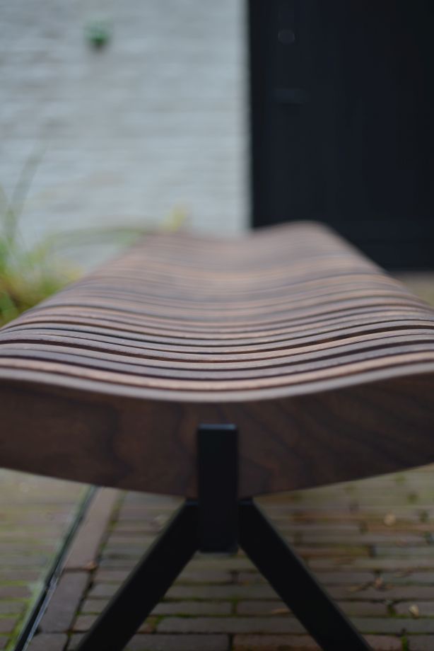 Detailaufnahme der Prelude Bank mit geschwungenen Holzlatten und schwarzem Metallgestell. Gartenmöbel für den Außenbereich.