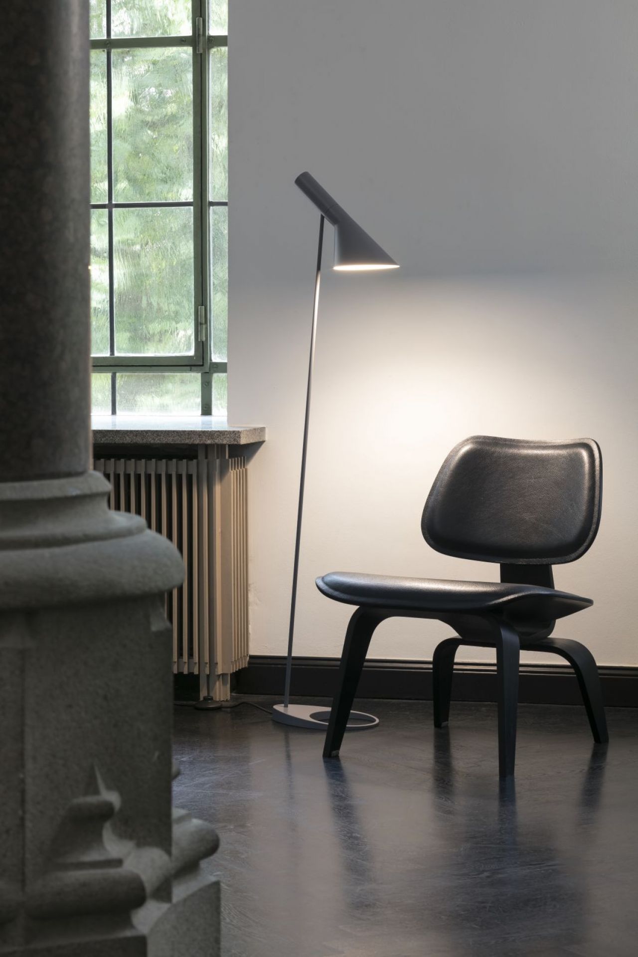 AJ Stehleuchte in Blass Petroleum von Louis Poulsen neben einem schwarzen Stuhl. Designleuchte.