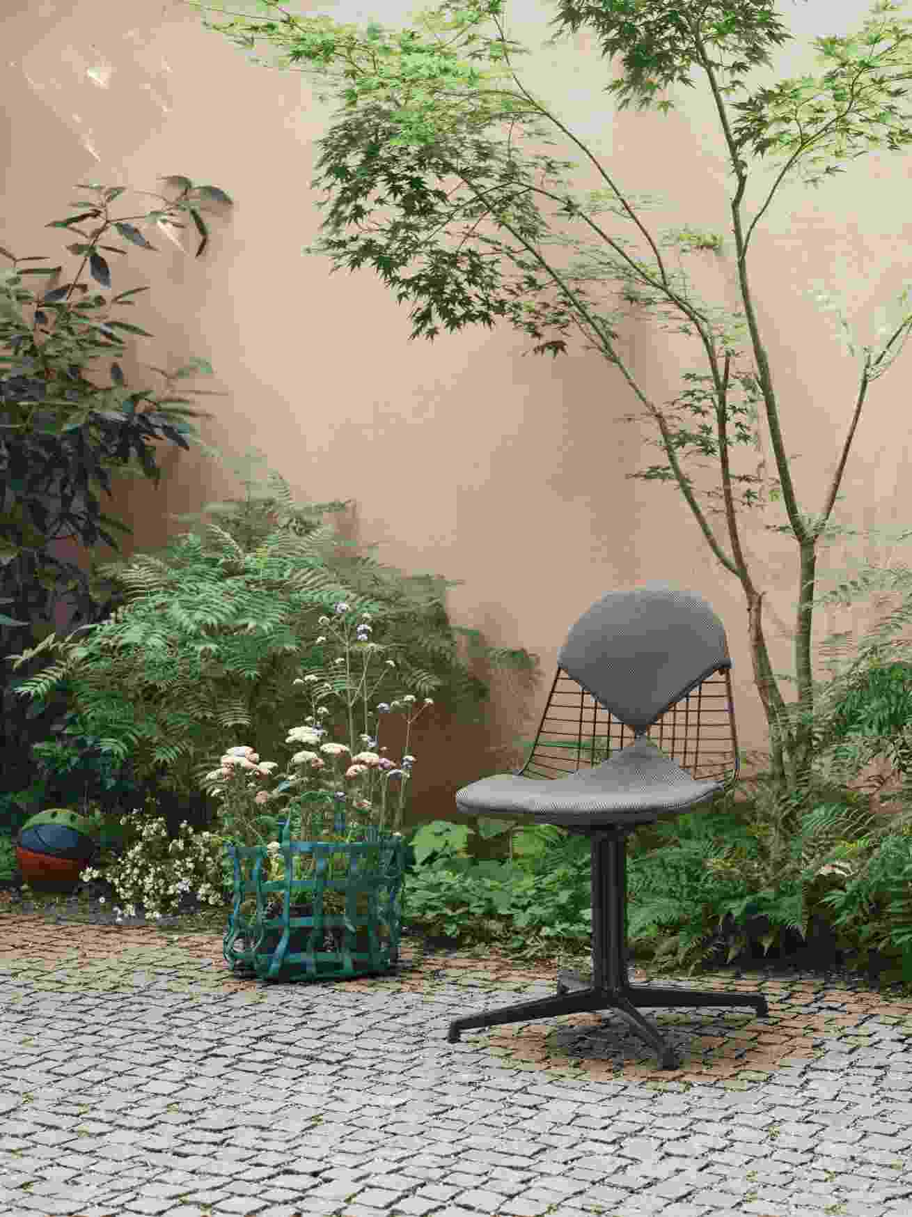 Vitra Wire Chair Bikini Outdoor Stuhl in Grau vor Gartenkulisse, Design Gartenmöbel.