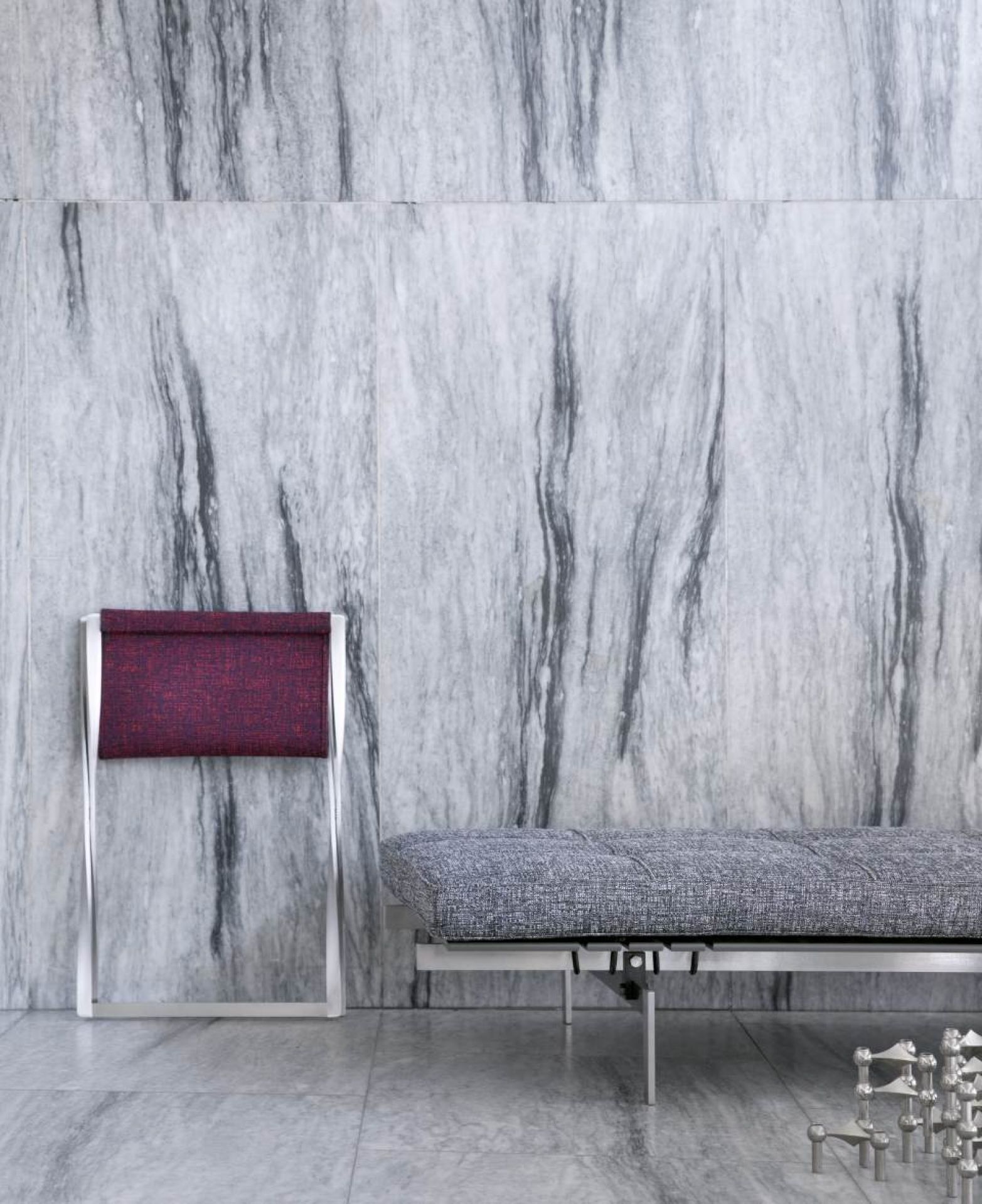 PK 80 Liege von Fritz Hansen mit grauem Bezug und passendem Hocker vor Marmorwand.