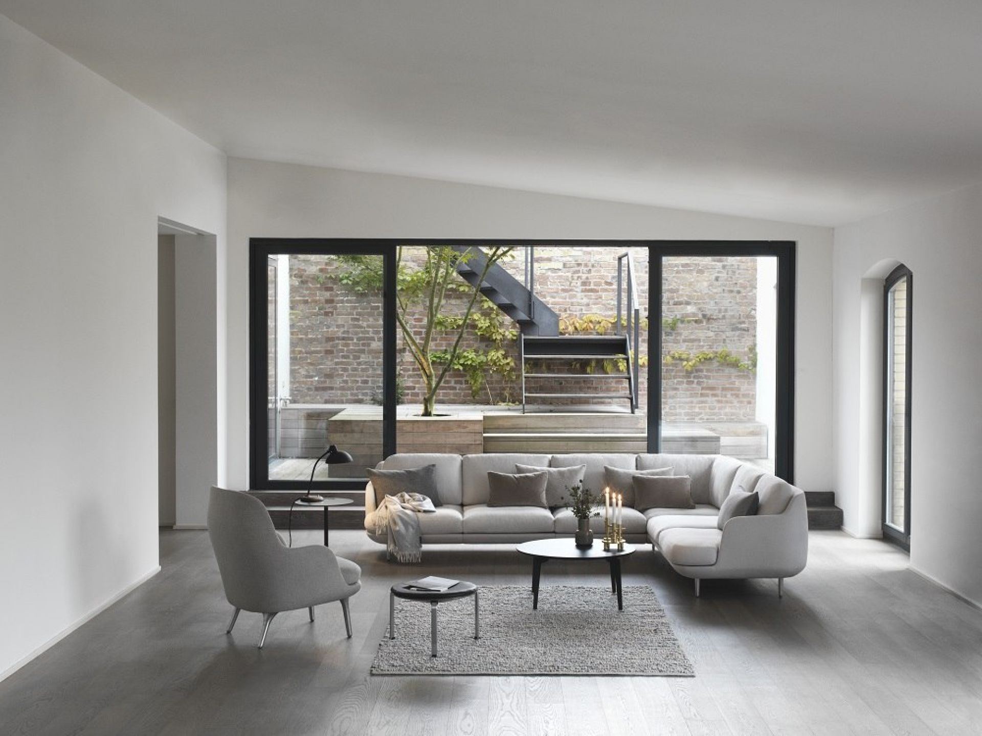 Heller Wohnraum mit grauem PK33 Hocker von Fritz Hansen, Sessel und großem Ecksofa.
