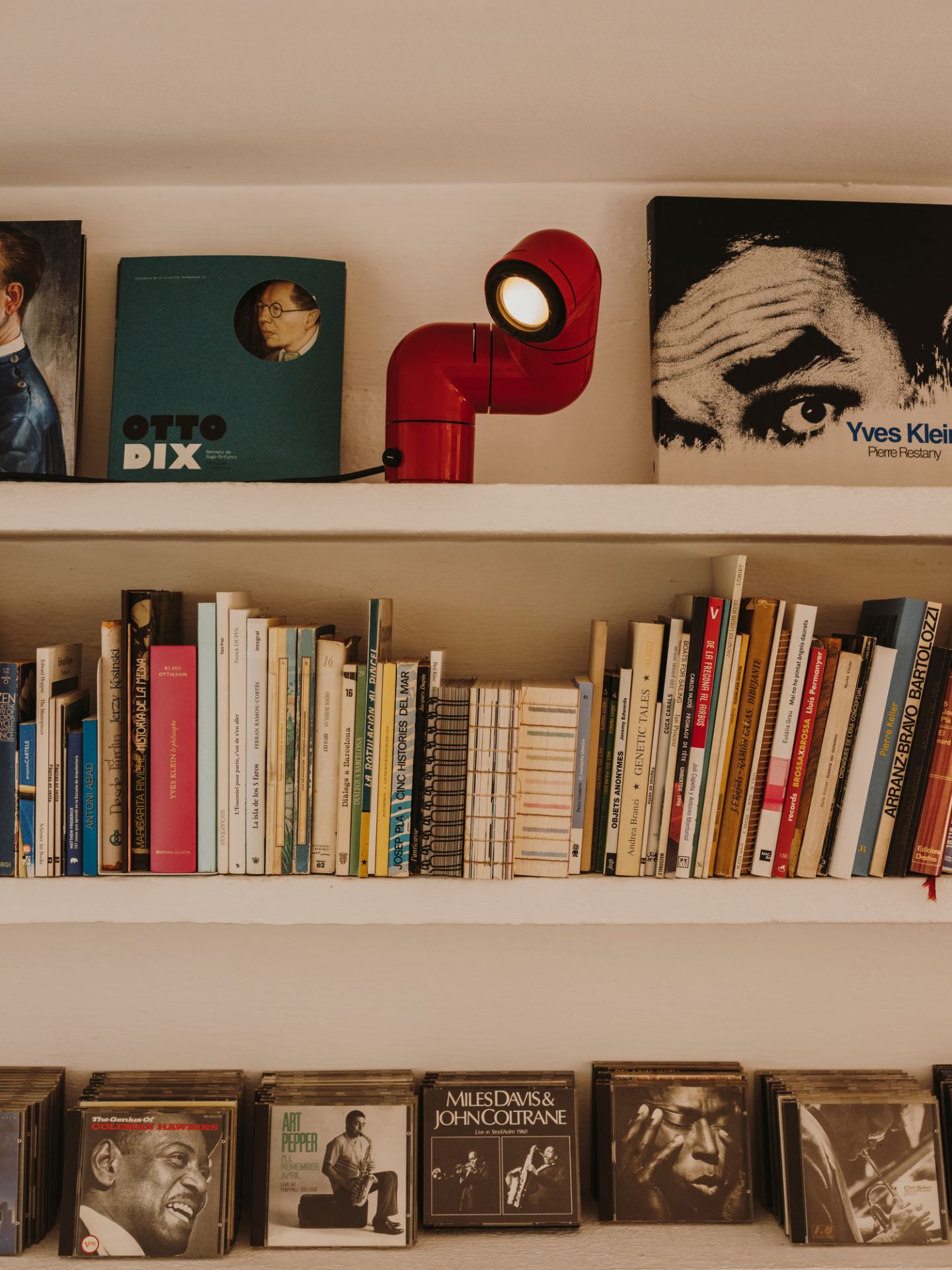 Rote Tatu Tischleuchte von Santa & Cole auf einem Bücherregal mit Büchern und Schallplatten.