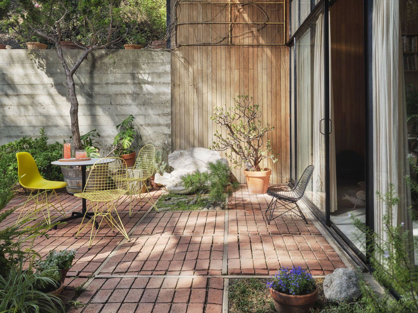 Gelbe und schwarze DKR Wire Chairs von Vitra mit Sitzkissen im Garten auf Backsteinboden.