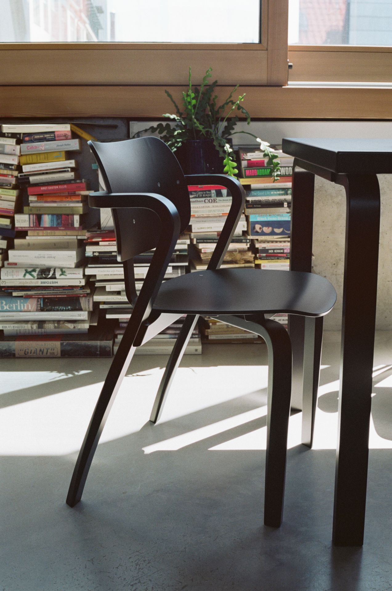 Schwarzer Aslak Chair Stuhl von Artek vor Bücherwand und Fenster, modernes Möbeldesign für Wohnzimmer und Büro.