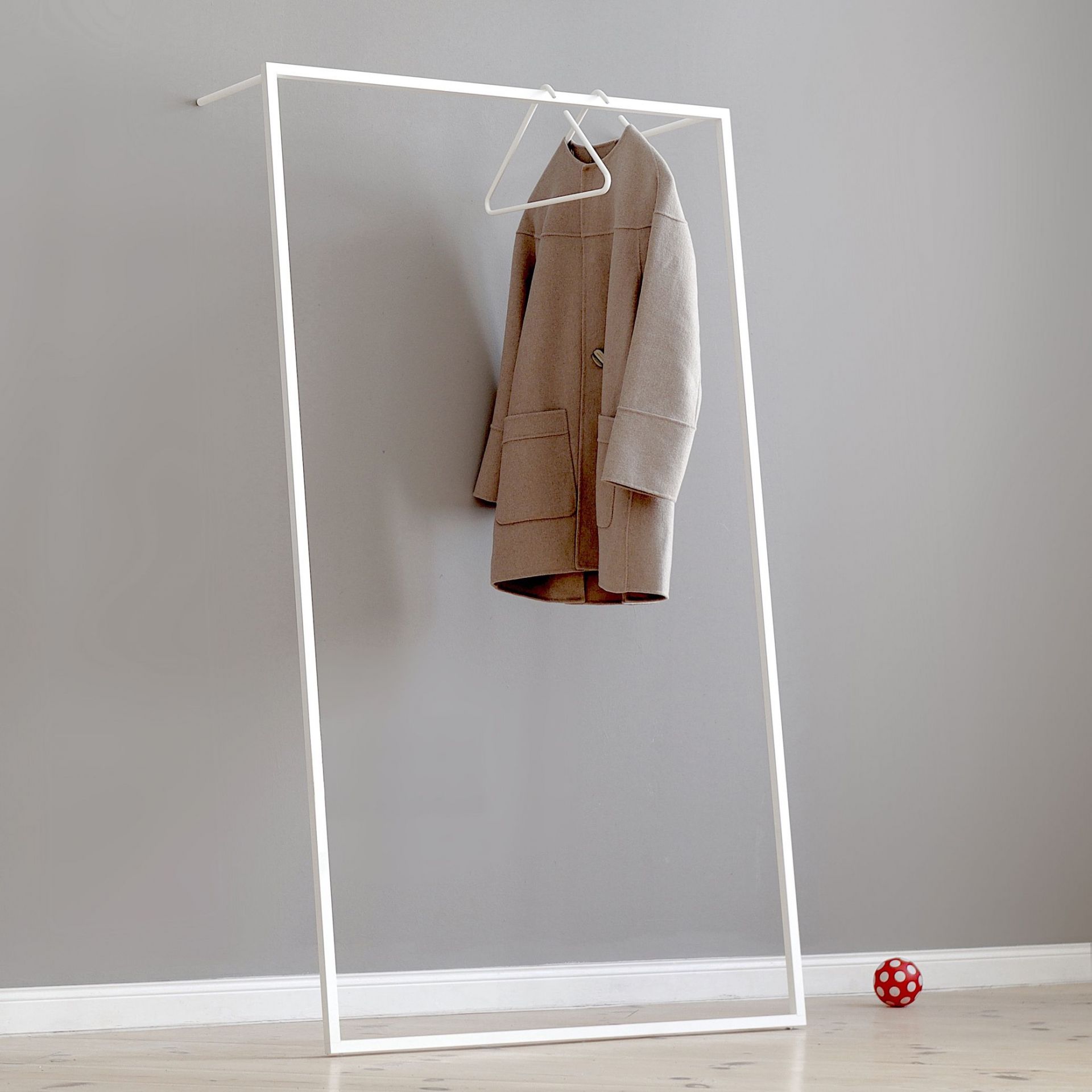 Weiße Leano Anlehngarderobe von Roomsafari mit Mantel an Kleiderbügel vor grauer Wand. Moderne Garderobenlösung.
