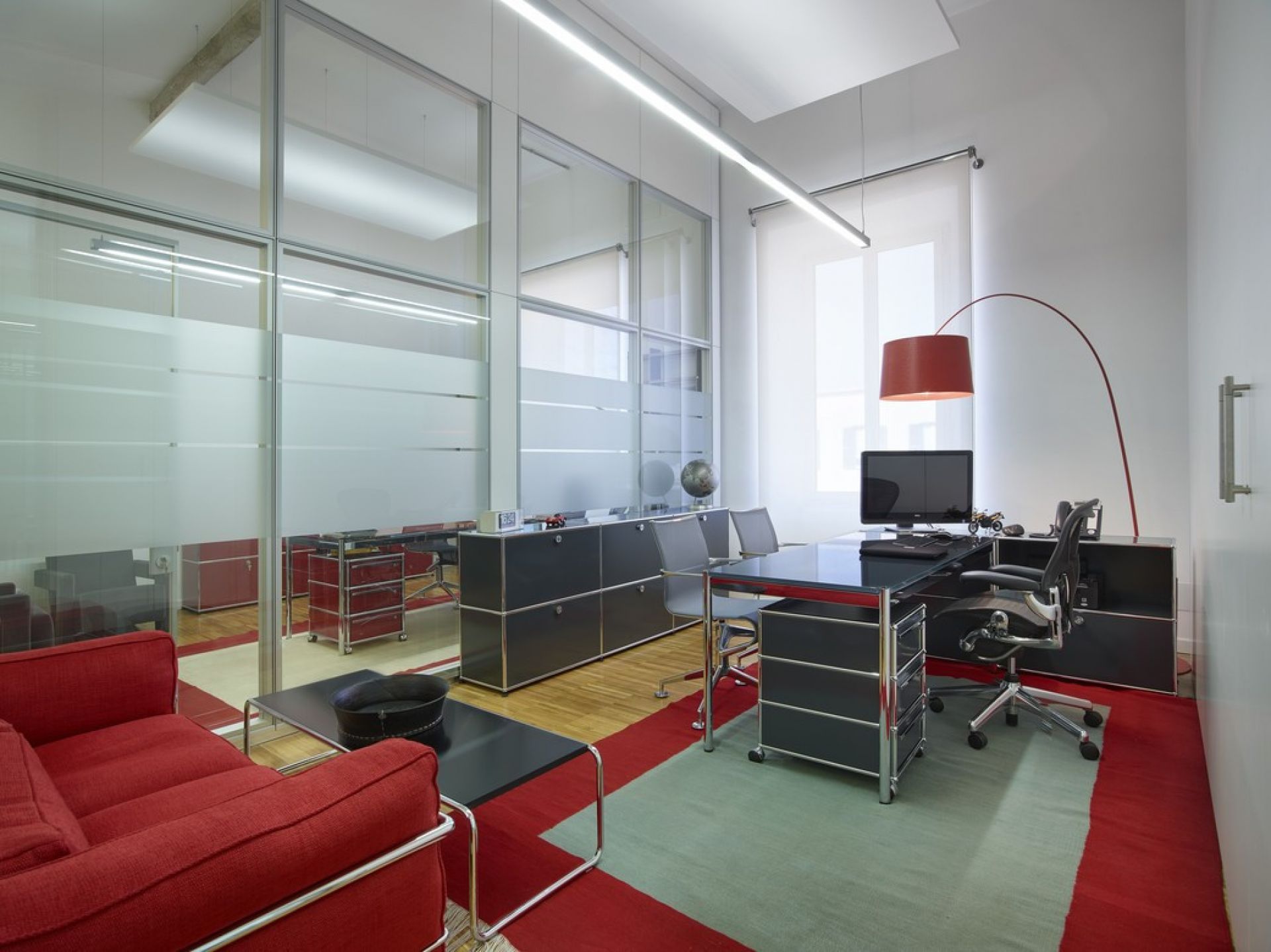 Helles Büro mit USM Haller Tisch, Sideboard und rotem Sofa für modernes Wohnen und Arbeiten.