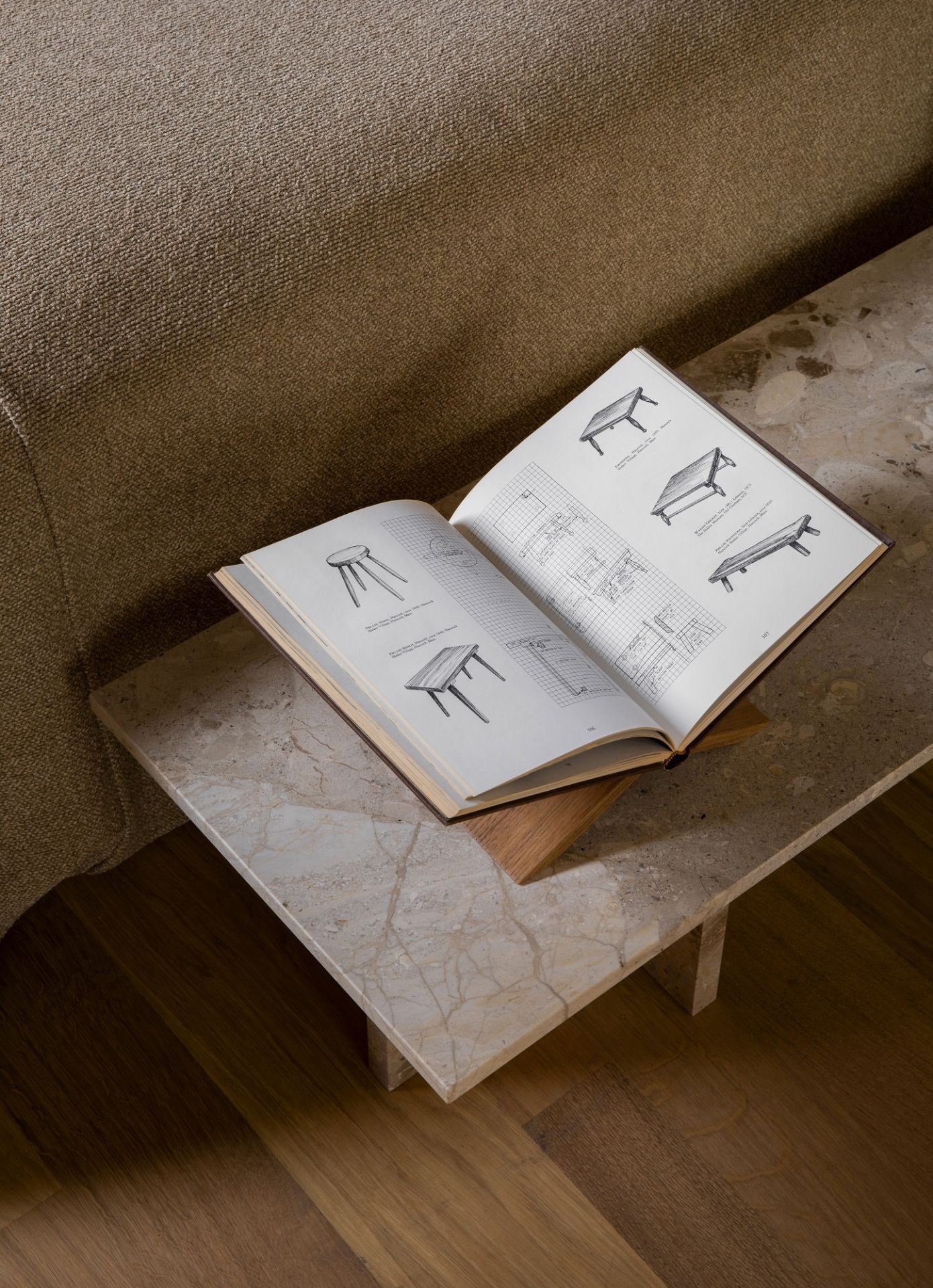 Androgyne Couchtisch von Audo Copenhagen aus Marmor mit Buch über Tischdesign neben Sofa.