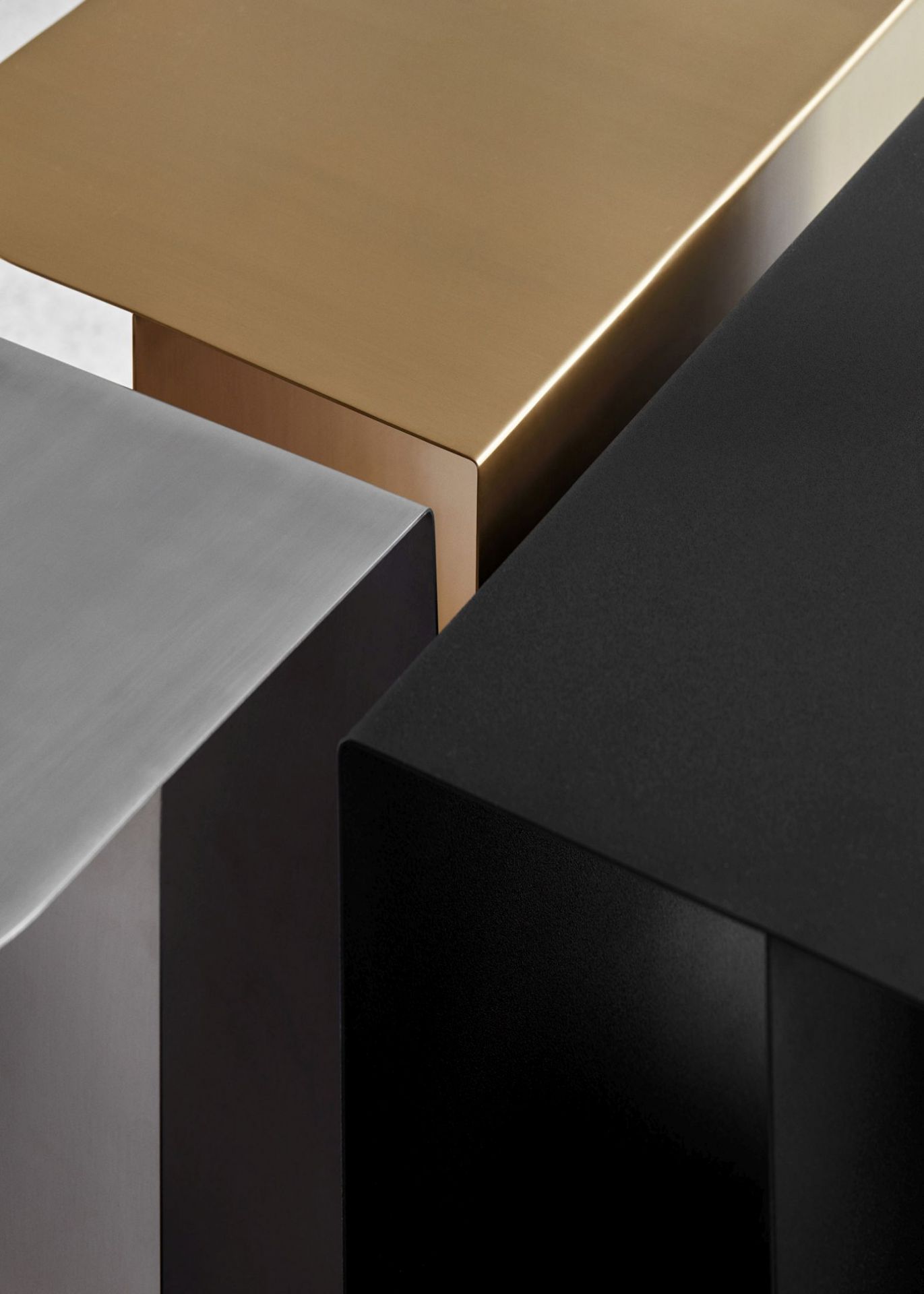 Detailaufnahme von drei Mass Beistelltischen aus Stahl in Schwarz, Gold und Silber.