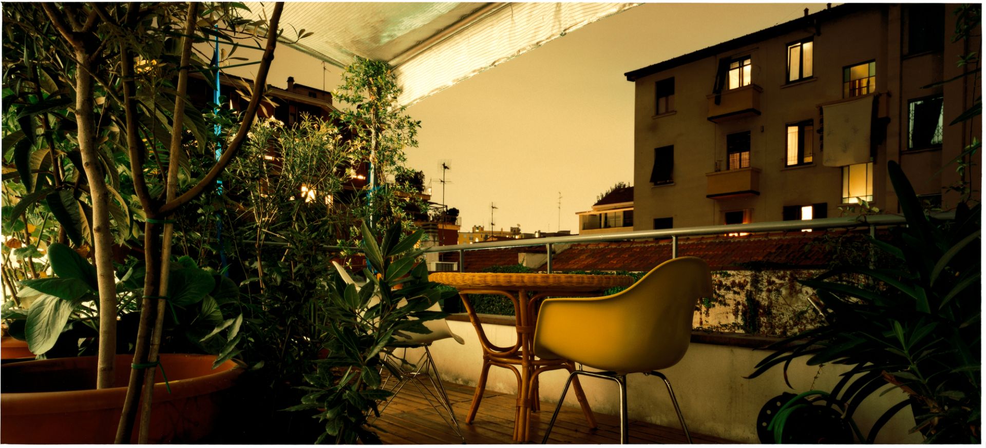 Gelber Eames Plastic Arm Chair DAR Stuhl von Vitra auf einem begrünten Balkon bei Nacht.