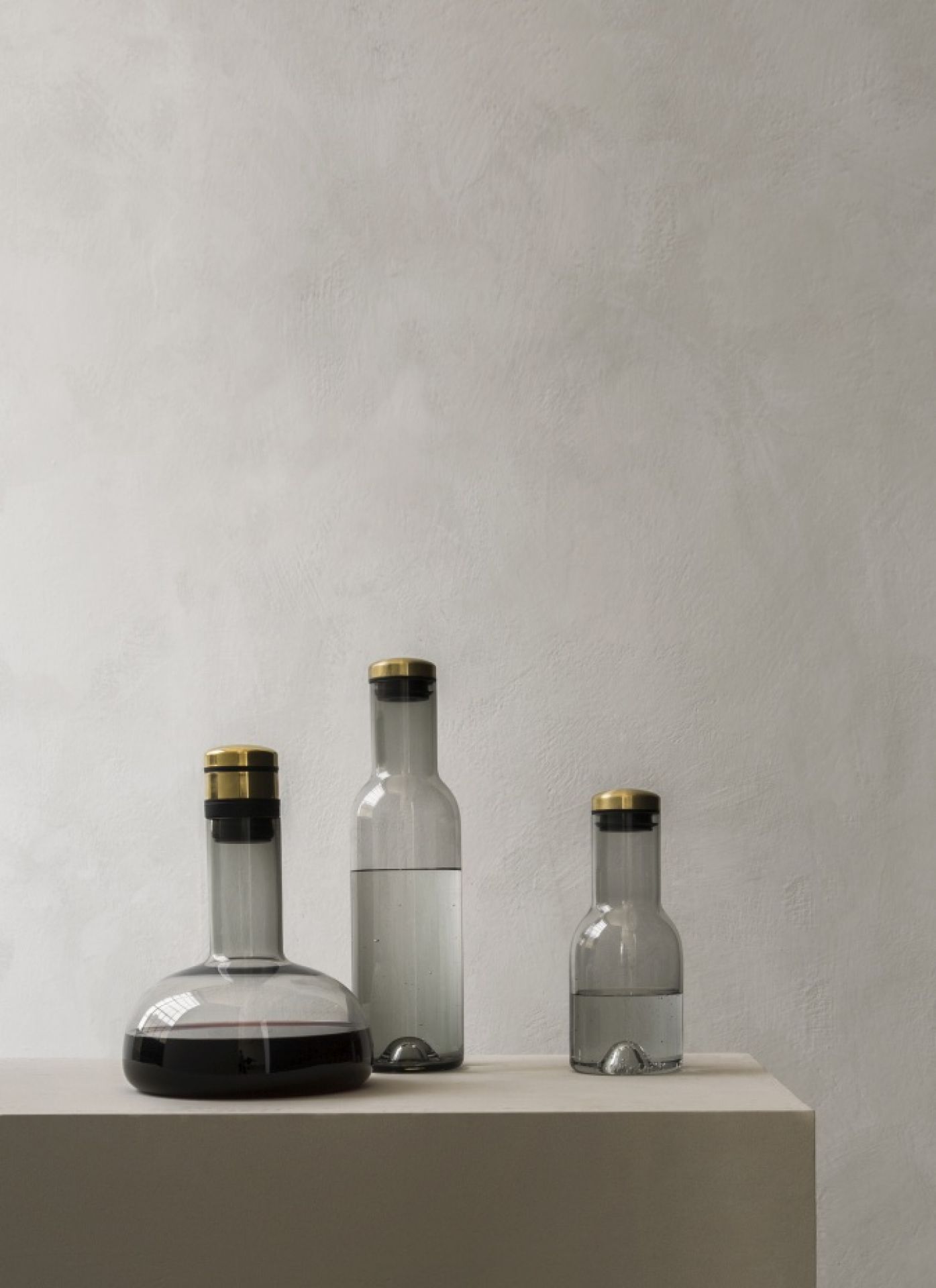 Wine Breather Collection: Drei graue Glaskaraffen mit goldenen Deckeln, eine mit Rotwein gefüllt, auf einem Podest.