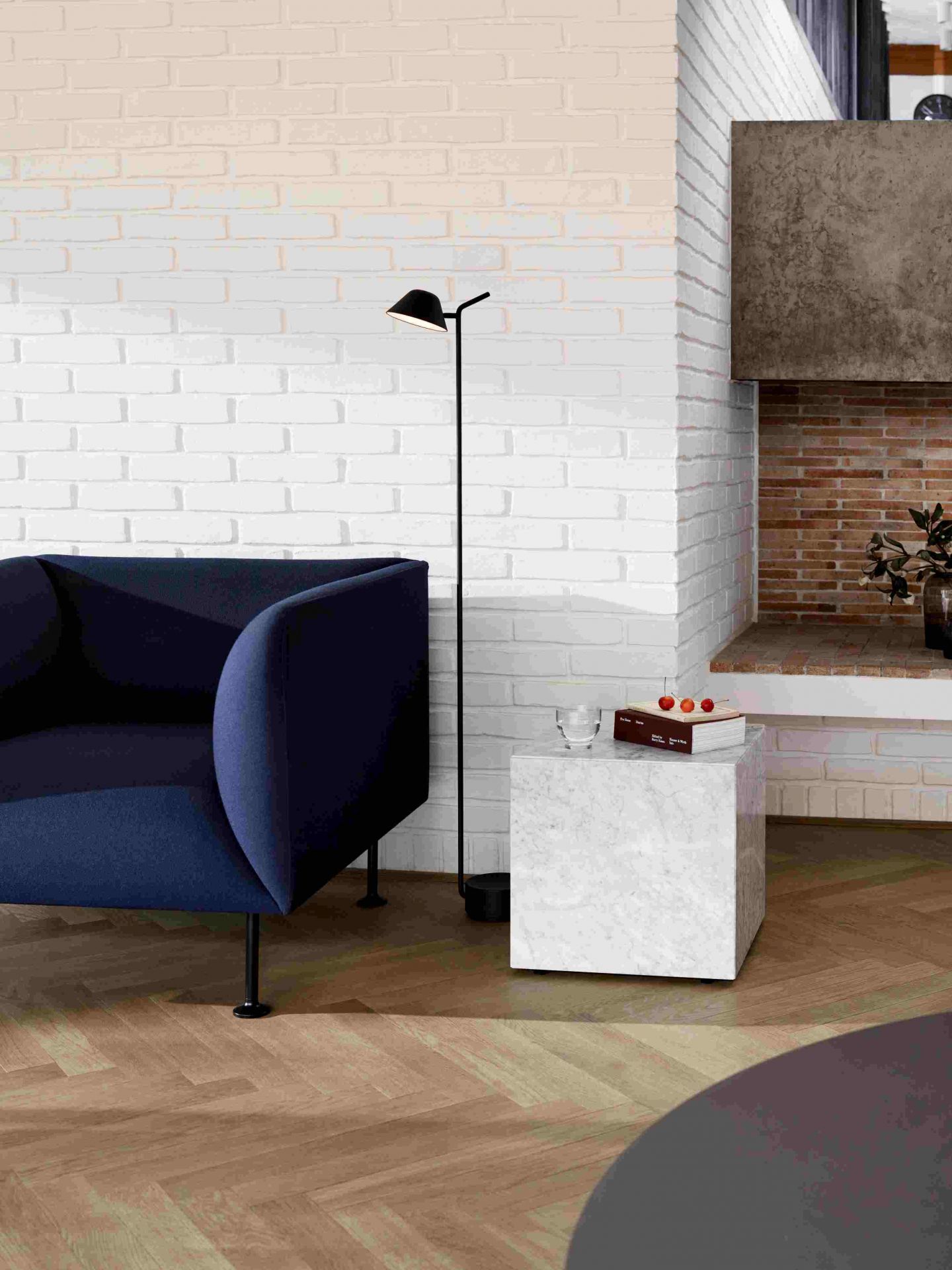 Audo Copenhagen Plinth Tisch aus Marmor neben blauem Sessel und Stehlampe im Wohnzimmer.