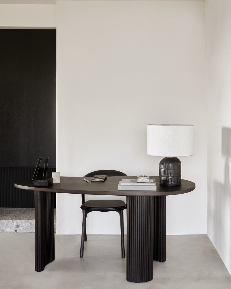 Ethnicraft Boomerang Schreibtisch aus dunklem Mahagoni-Holz mit passendem Stuhl und Lampe im minimalistischen Interieur.