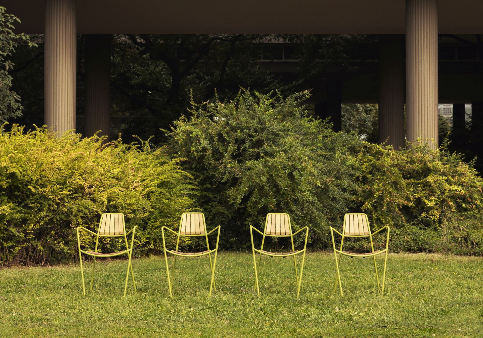 Vier Osmo Outdoor Stühle von Prostoria in Grün auf Rasen vor Büschen und Säulen.