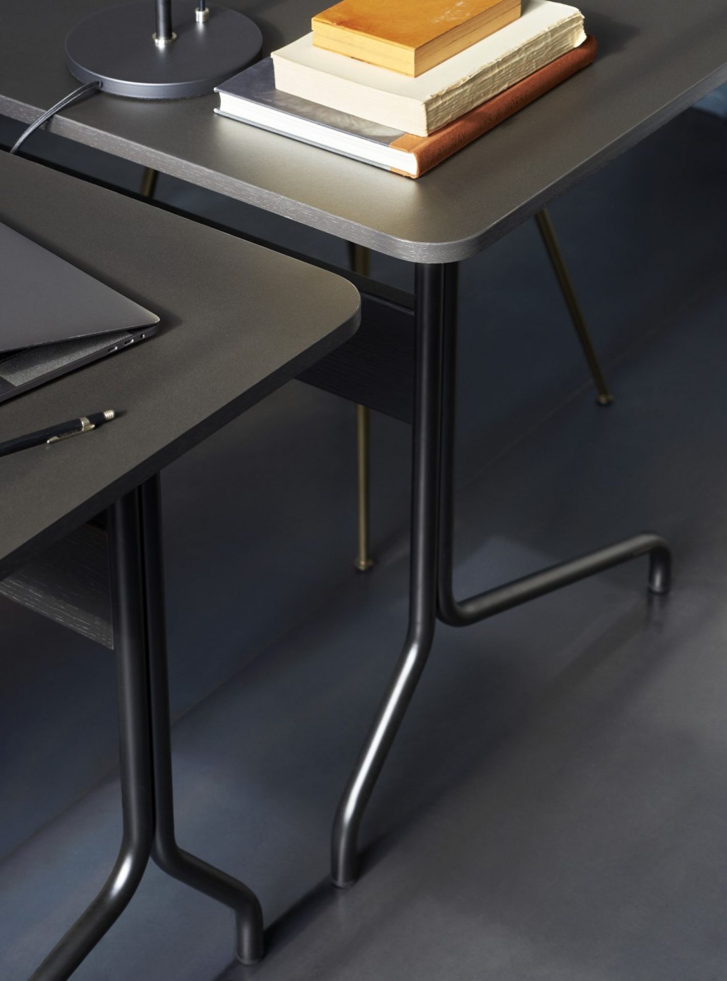 Detailaufnahme des AndTradition Pavilion Schreibtischs in Grau mit Laptop, Stift und Bücher auf der Tischplatte.