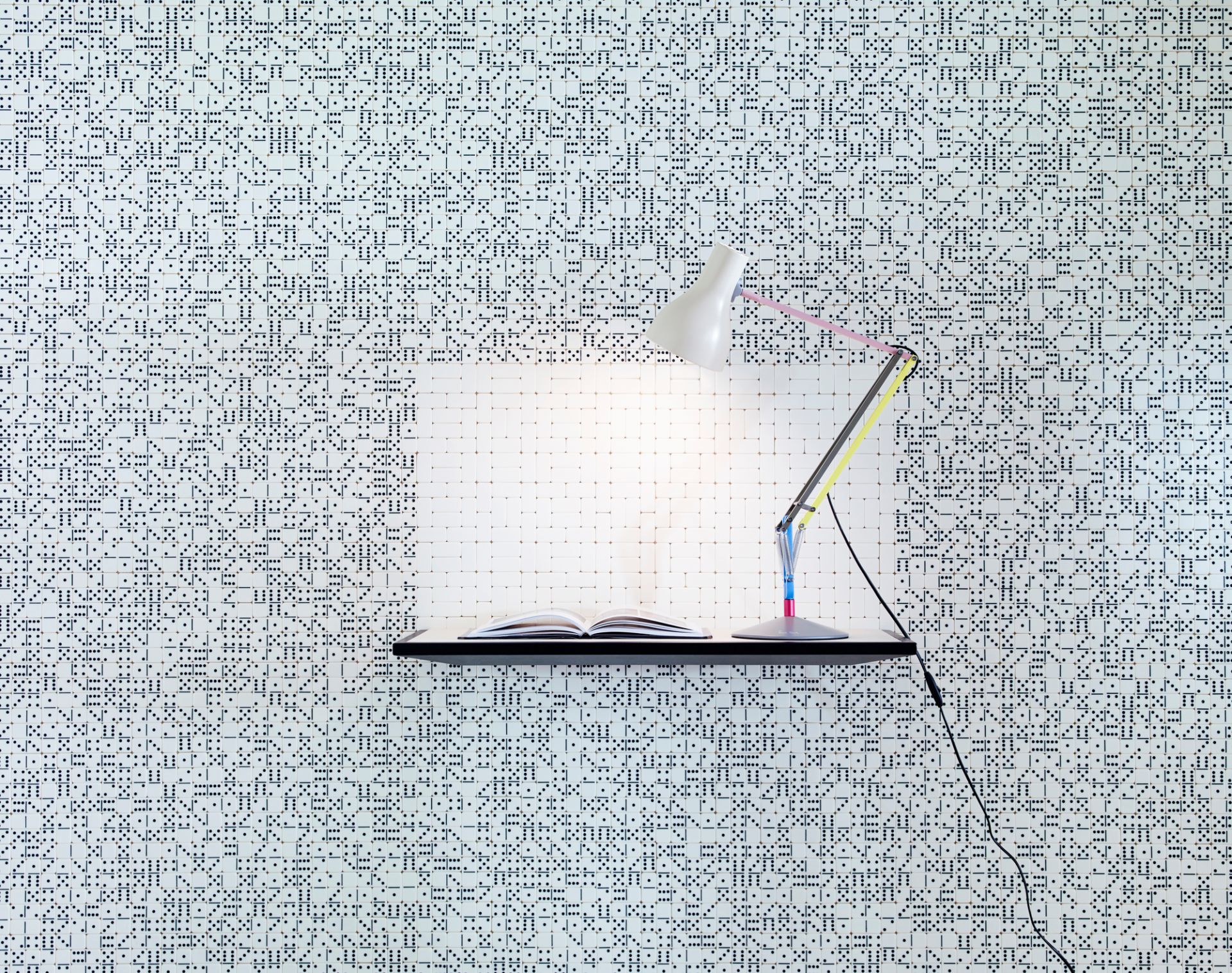 Anglepoise Type 75 Mini Paul Smith Edition Tischleuchte auf Regal mit offenem Buch vor gemusterter Wand.