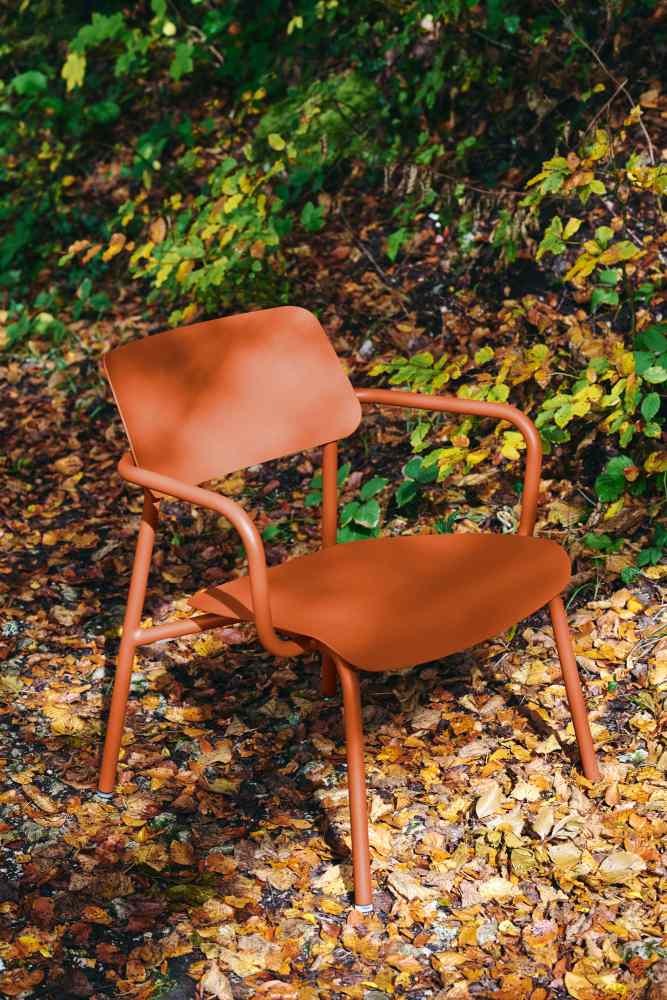Fermob Studie Lounge Sessel Outdoor in Rostrot auf herbstlichem Laub, ideal für Garten und Terrasse.