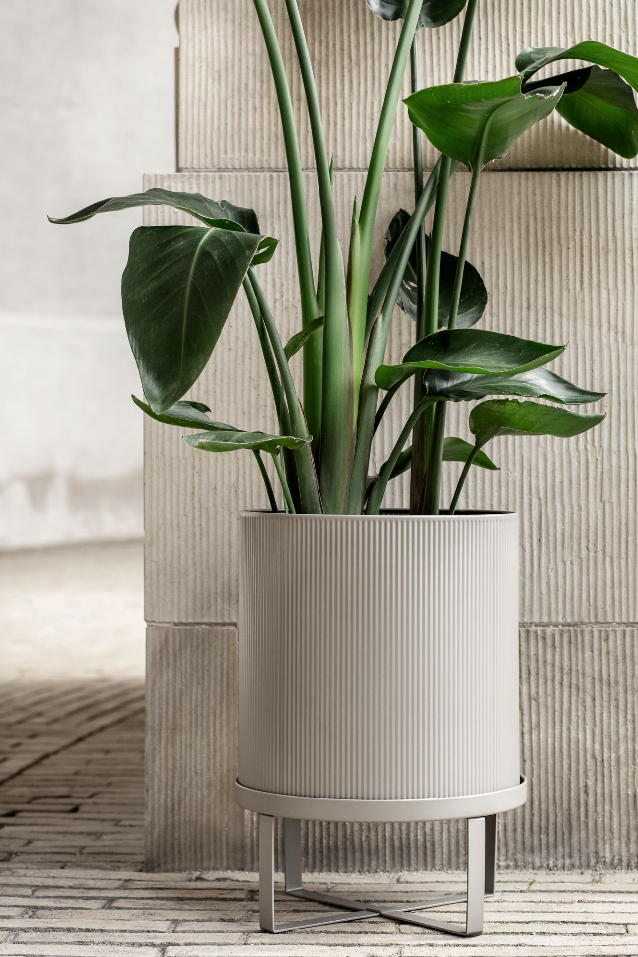 Großer, gerippter, grauer Ferm Living Blumentopf der Serie Bau Pot mit grüner Pflanze auf einem grauen Untergestell.