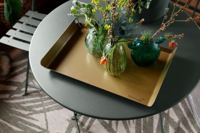 Nahaufnahme eines grauen Fermob Bistro Tisches im Freien mit goldenem Tablett und Vasen.