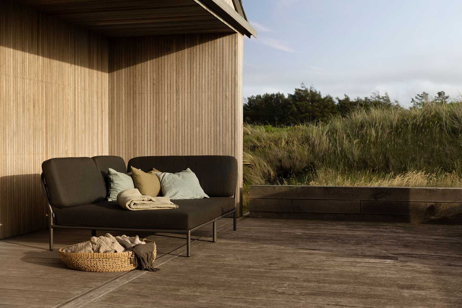 Level Cozy Corner Outdoor Sofa, linke Ecke, mit Kissen und Decke auf Holzterrasse.