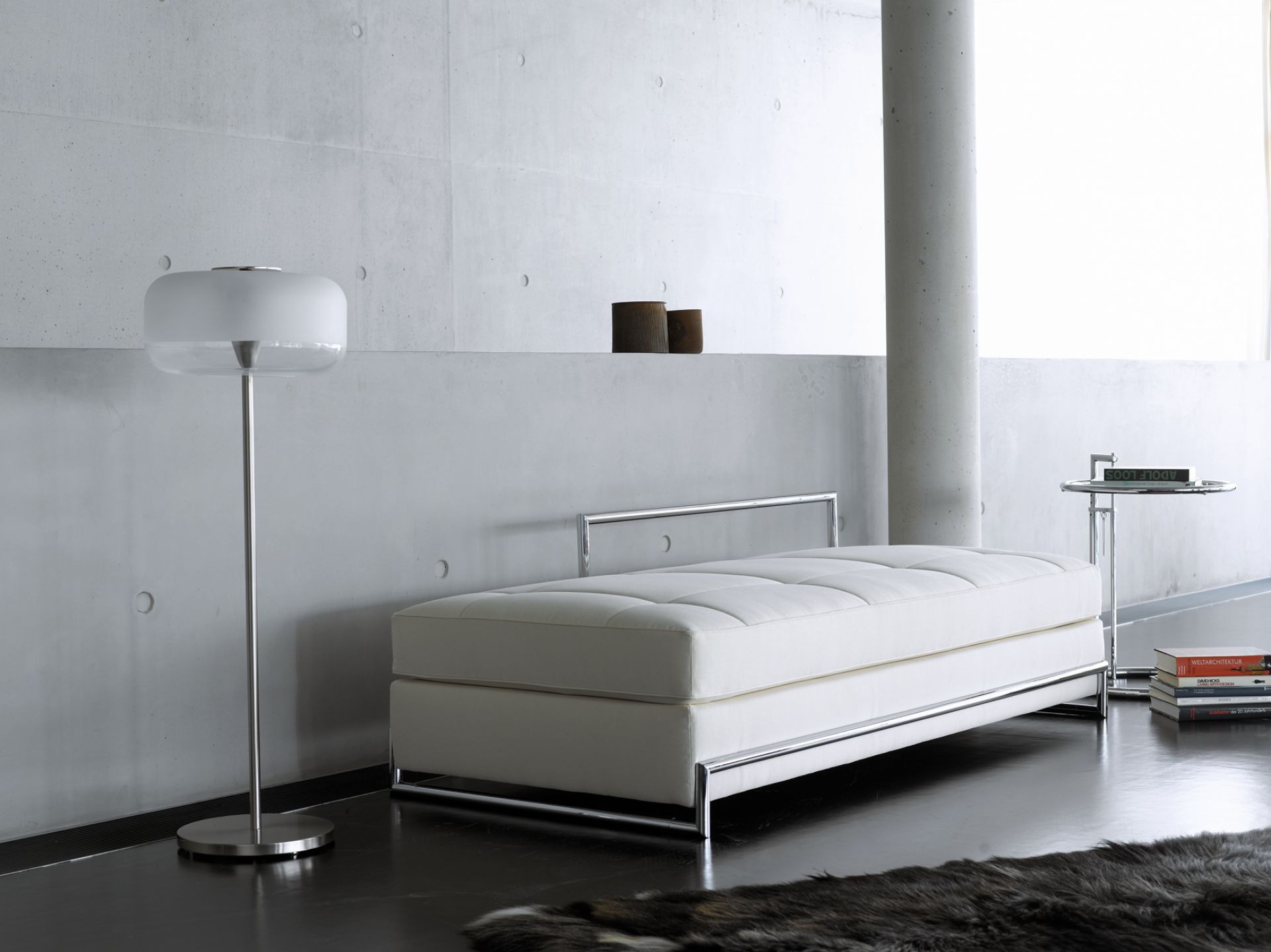 Adjustable Table E1027 Beistelltisch von ClassiCon neben weißer Ottomane und Stehlampe im modernen Interieur.